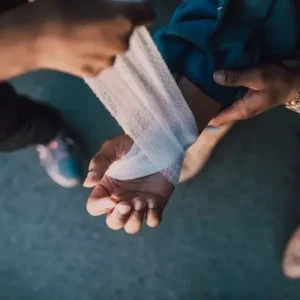 Close up of two sets of hands. The first person is bandaging the hand of the second person.